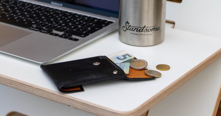 A laptop, a metal bottle, and an open wallet with coins and cash on a wooden tray.