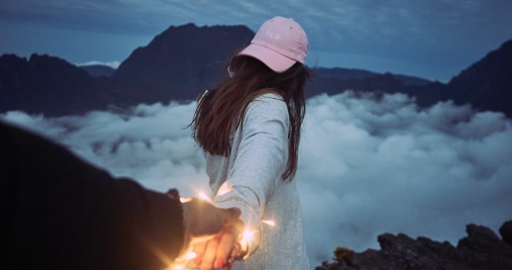 woman holding person's hand in front of clouds