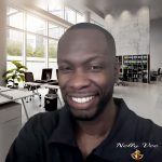 A smiling man in a black shirt with a modern office background, featuring plants, desks, and a bookshelf.